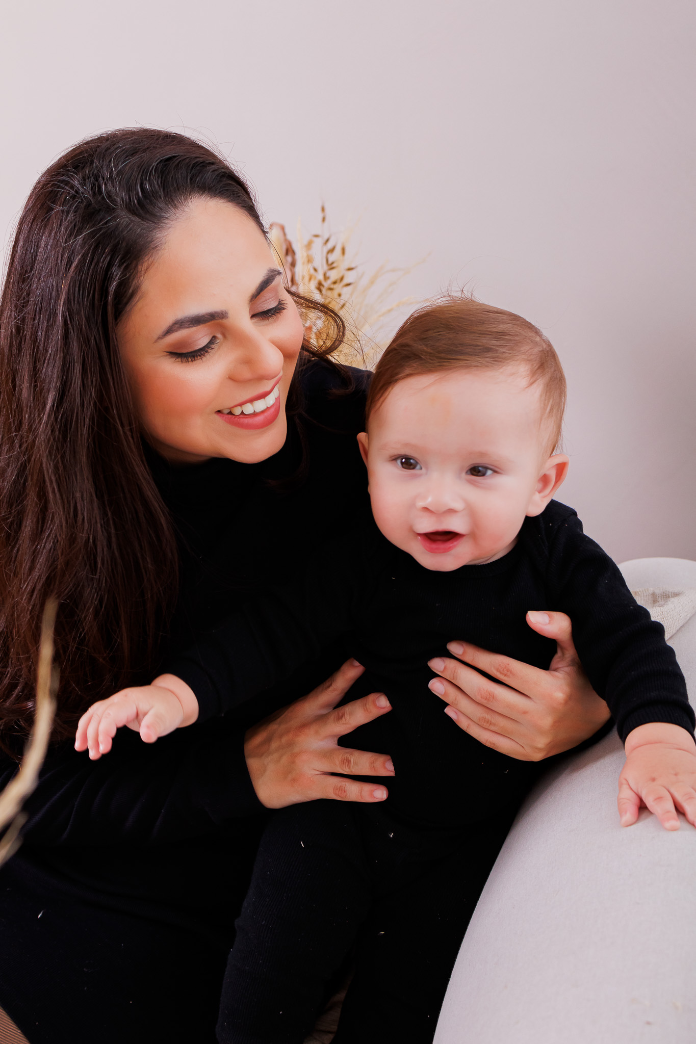 Todos pela acessibilidade: A mãe segura a filha no colo, com ambas olhando diretamente para a câmera. A iluminação de estúdio foi cuidadosamente ajustada para destacar os traços e sorrisos, enquanto o fundo neutro enfatiza a conexão íntima. A qualidade da imagem reflete a habilidade da fotógrafa em captar emoções com precisão.